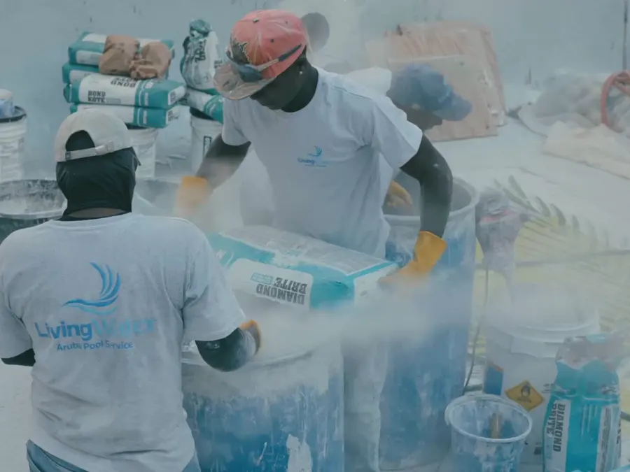 Two Living Water Aruba technicians in company shirts mixing material during a pool renovation