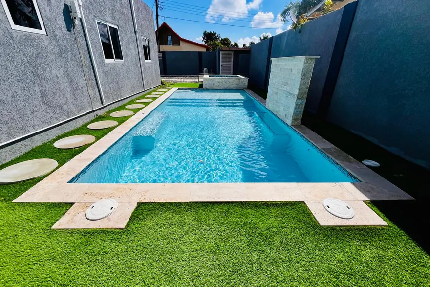 A clean, clear pool with a stone deck and artificial lawn